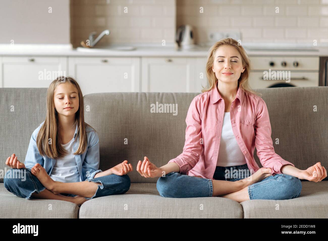 Mamma e figlia meditano. Bella mamma caucasica giovane con carina piccola figlia che fa yoga e meditazione a casa sul divano, seduta in posizione di loto, calma, relax Foto Stock