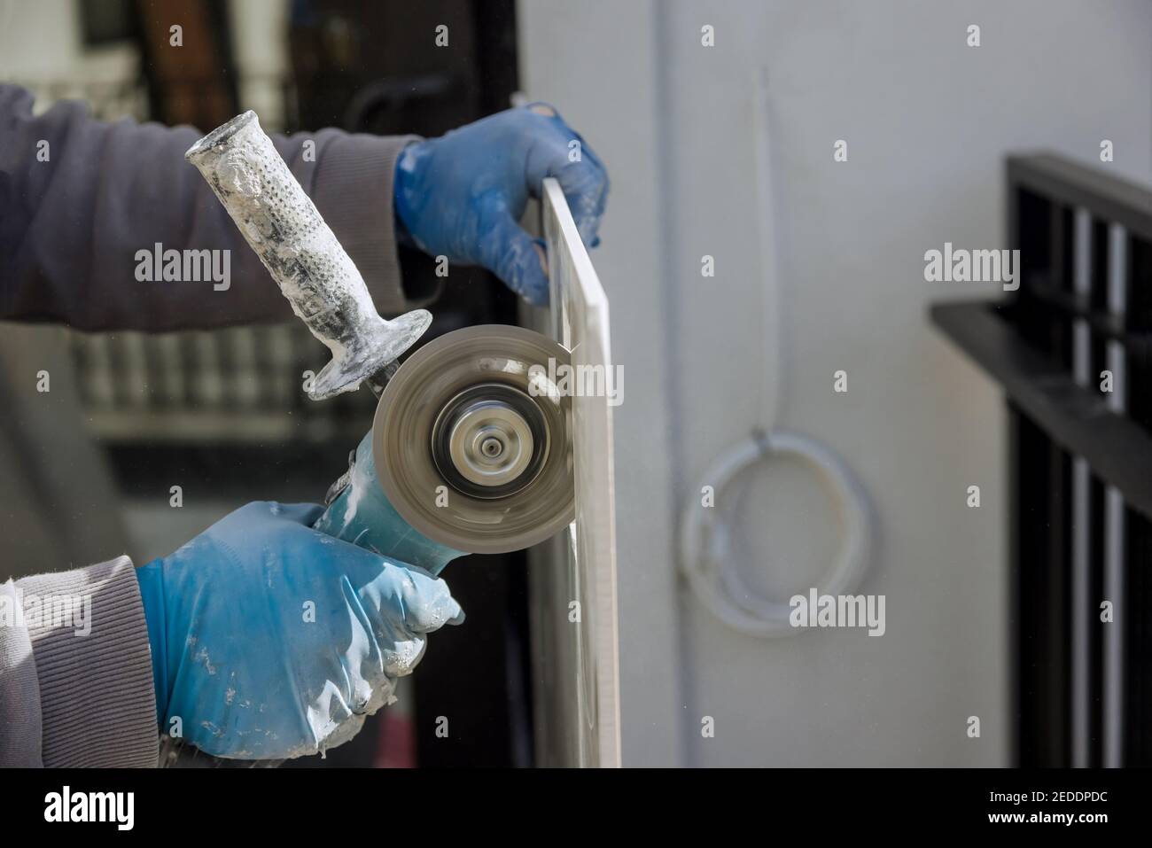 Uomo che taglia il foro quadrato per la presa elettrica nella piastrella sagomare utilizzando utensili elettrici smerigliatrici angolari Foto Stock