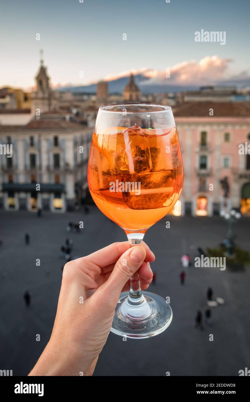 Donna che porta il bicchiere di Aperol Spritz con vista sulla città di Catania in Sicilia, Italia Foto Stock