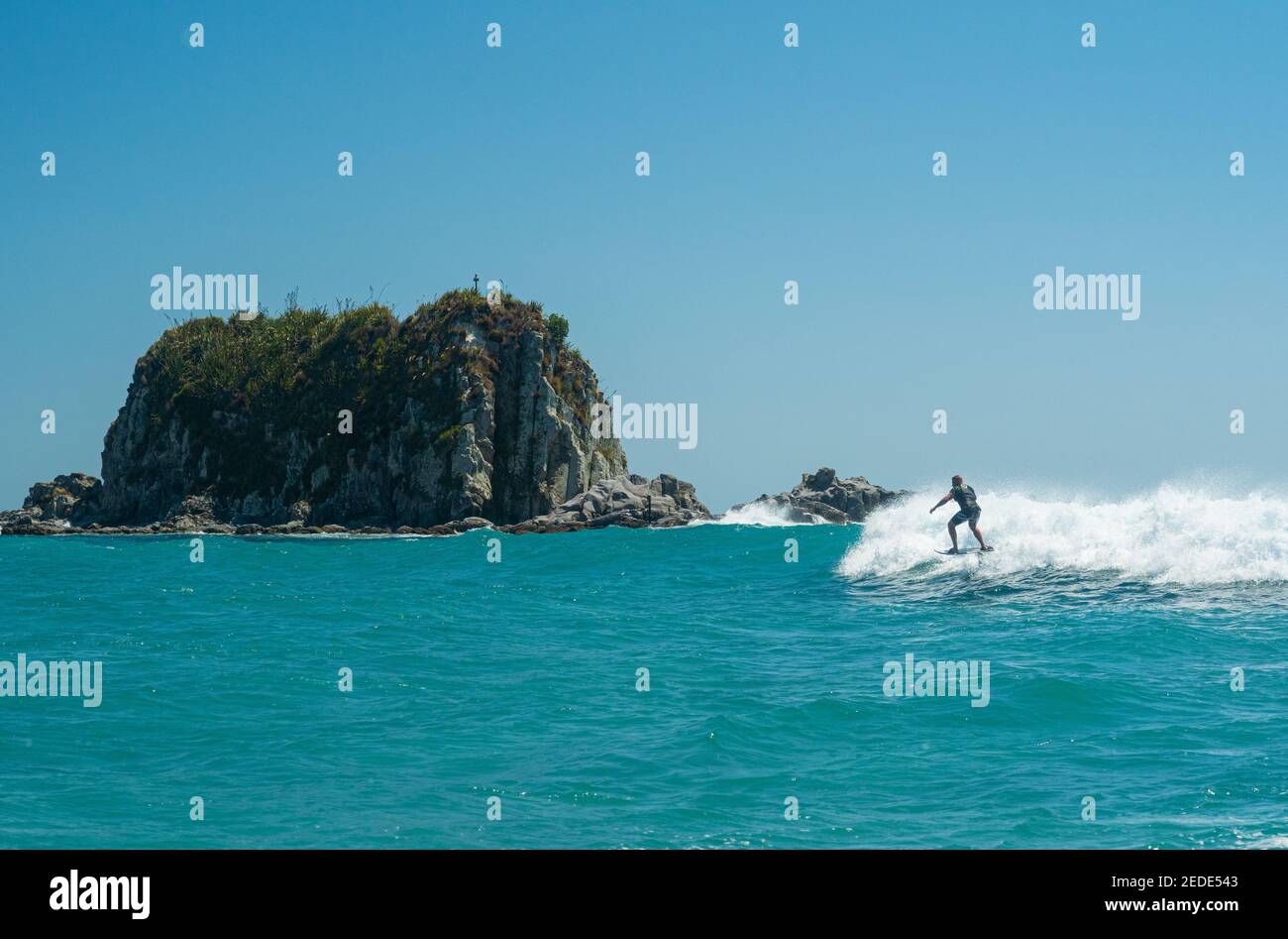 Un uomo surfs su un aliscafo surf sulle onde turchesi a Mangawhai Heads, Nuova Zelanda. Cielo blu chiaro. Foto Stock