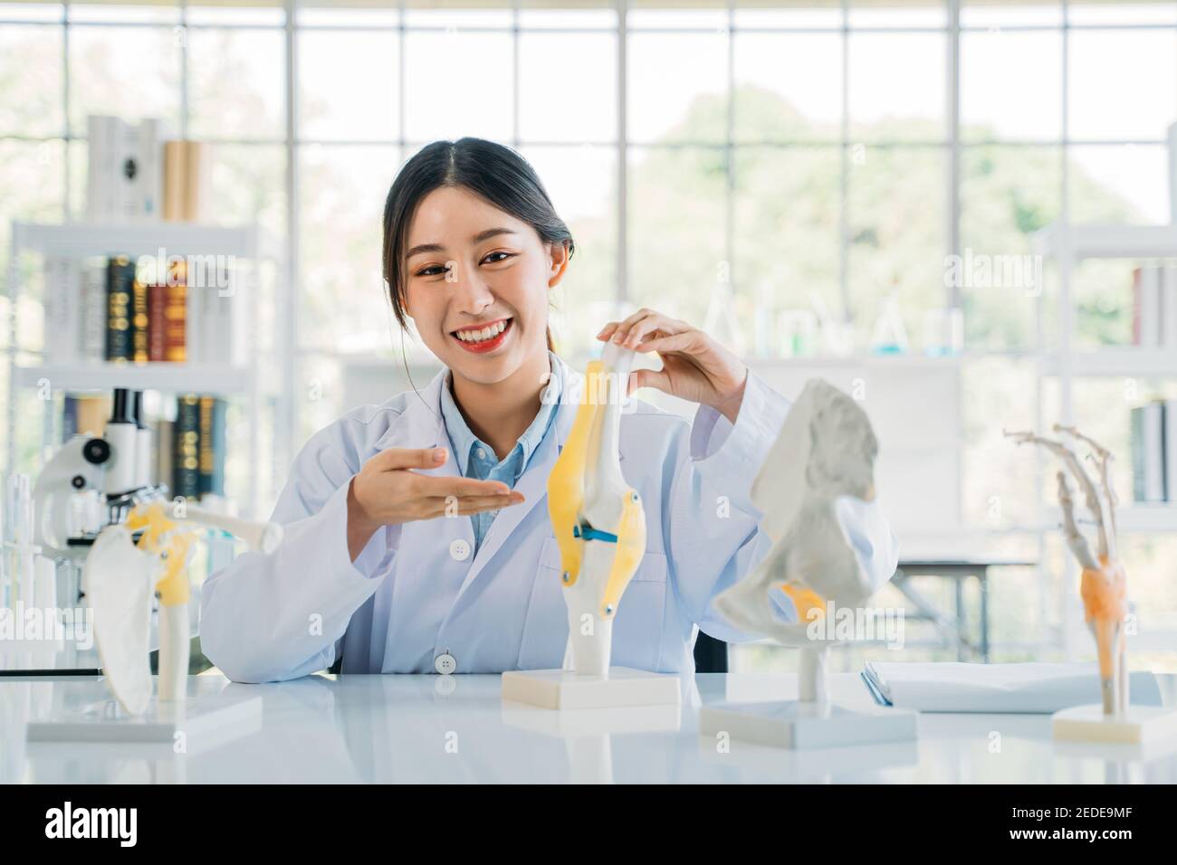 Ritratto di giovane donna asiatica medico indossando labcoat preparazione di un modello osseo mentre si spiega l'anatomia in ospedale per un video blog Foto Stock