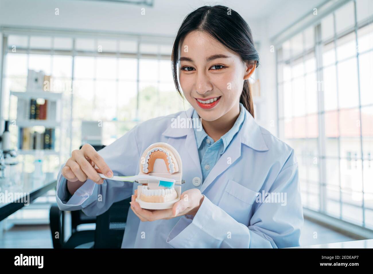 Ritratto di bella giovane dentista asiatico femminile che dimostra il giusto modo per spazzolare i denti tenendo il modello della bocca e lo spazzolino durante la registrazione video blog per l'insegnamento online Foto Stock