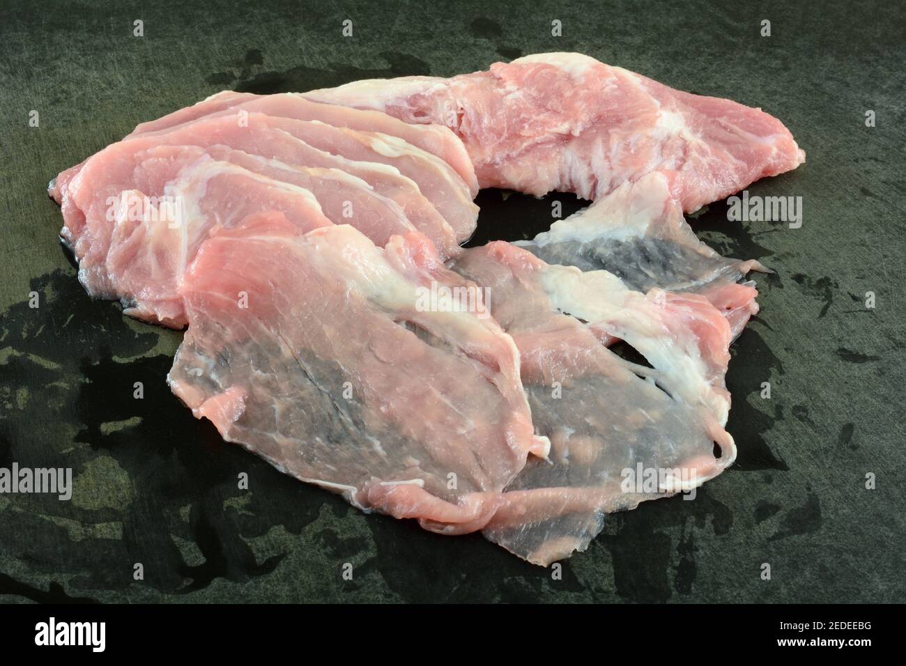Closeup di maiale crudo affettato sottile su taglio nero stagionato scheda Foto Stock
