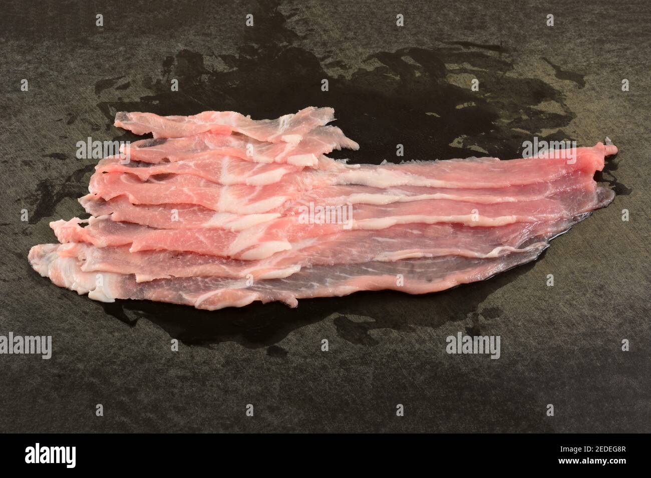 Closeup di maiale crudo affettato sottile su taglio nero stagionato scheda Foto Stock