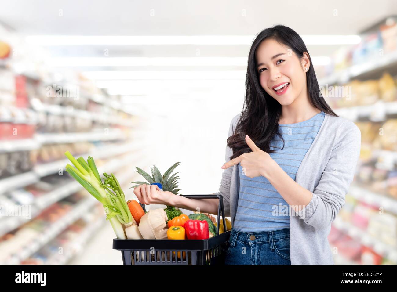 Bella donna asiatica tenendo carrello di shopping pieno di verdure e. generi alimentari nel supermercato Foto Stock