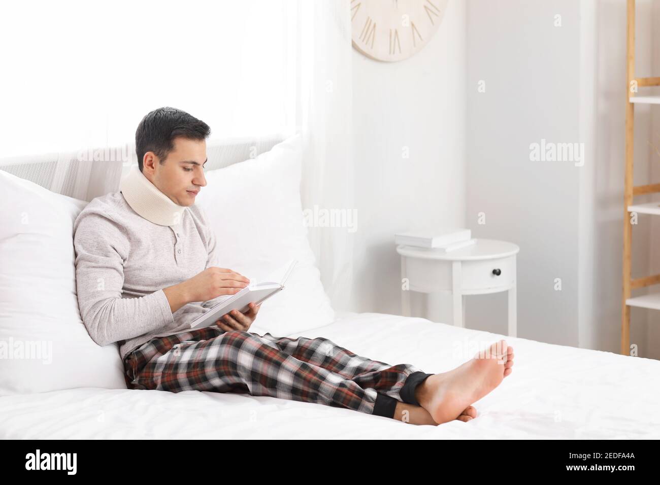 Giovane uomo con collare cervicale sul collo leggere libro a. casa Foto Stock