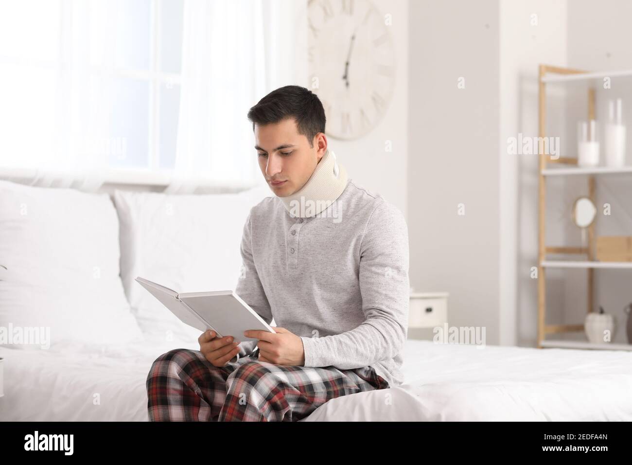 Giovane uomo con collare cervicale sul collo leggere libro a. casa Foto Stock