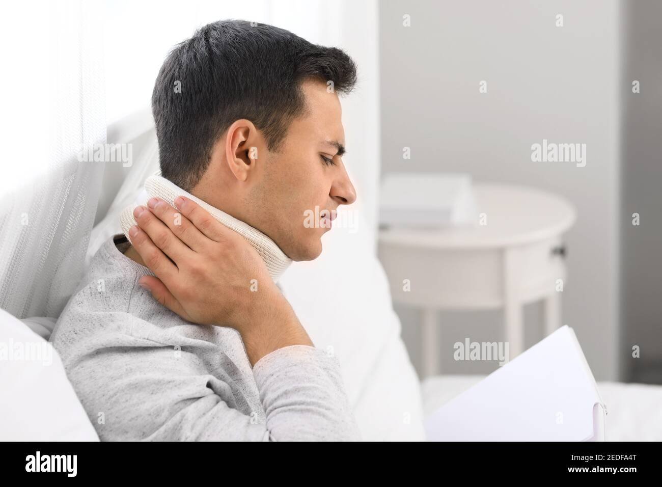 Giovane uomo con colletto cervicale sul collo che soffre di dolore a casa Foto Stock