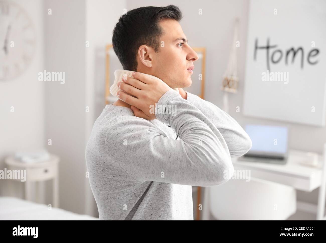 Giovane uomo con colletto cervicale sul collo che soffre di dolore a casa Foto Stock