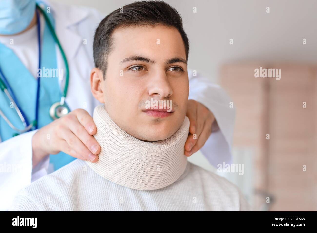 Medico che applica il collare cervicale sul collo del giovane uomo dentro clinica Foto Stock