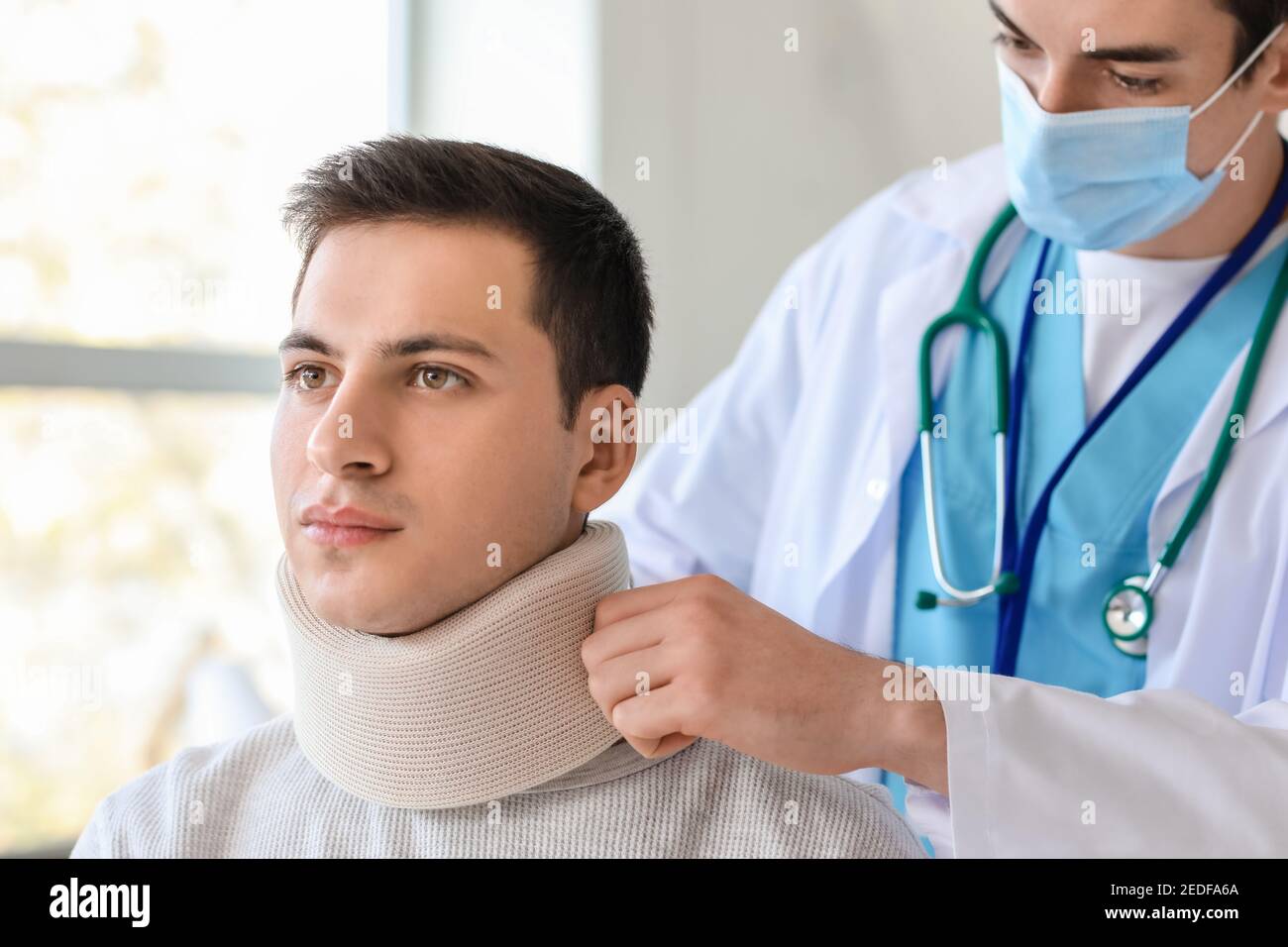 Medico che applica il collare cervicale sul collo del giovane uomo dentro clinica Foto Stock