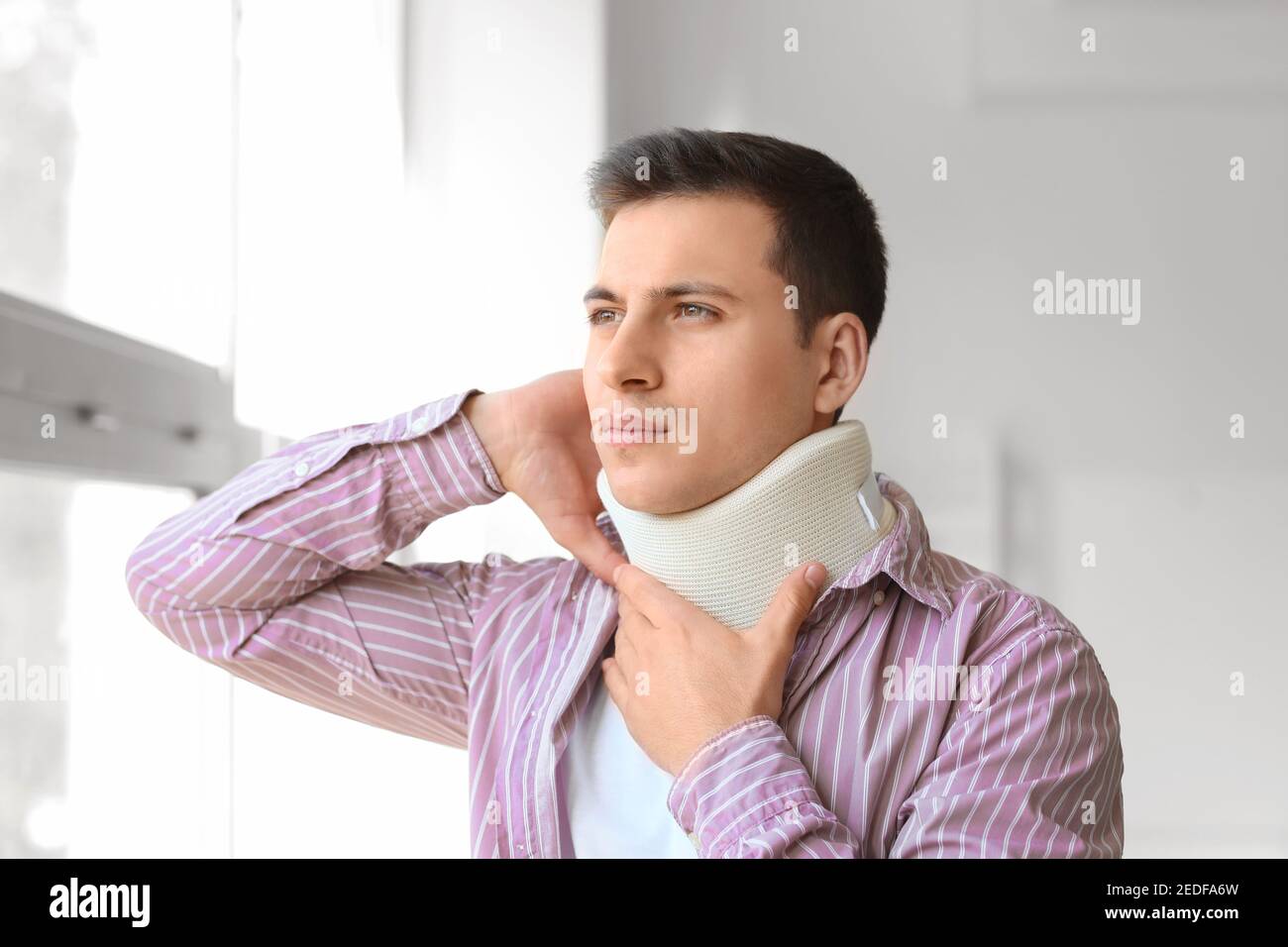 Giovane uomo con collare cervicale sul collo a casa Foto Stock