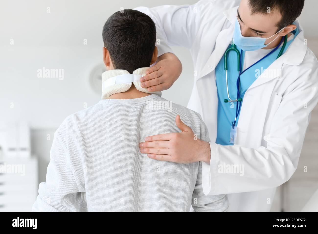 Medico che applica il collare cervicale sul collo del giovane uomo dentro clinica Foto Stock