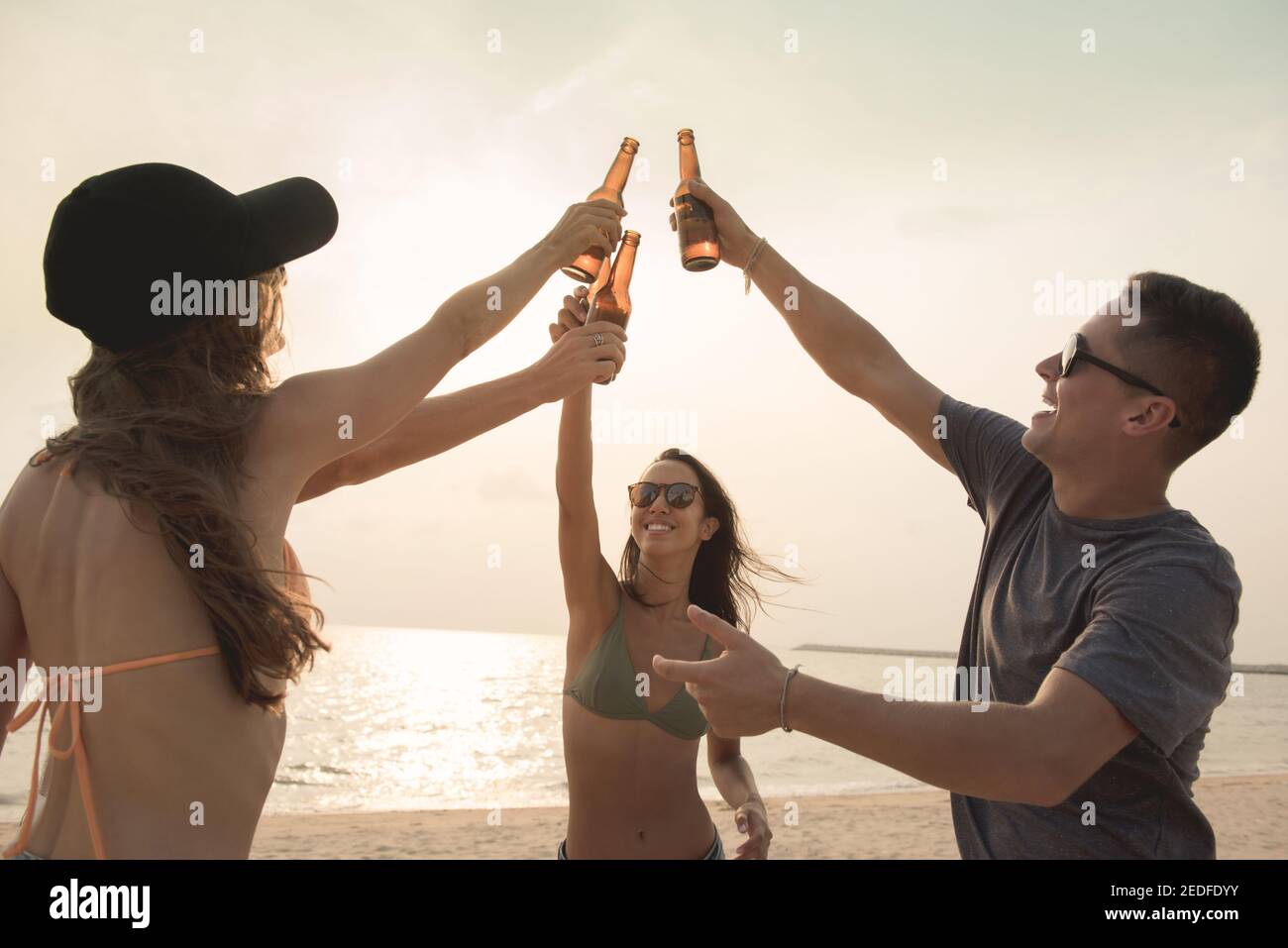 Gruppo di amici che hanno festeggiato festa claging bottiglie di birra fabbricazione un brindisi prima di bere in spiaggia al crepuscolo Foto Stock