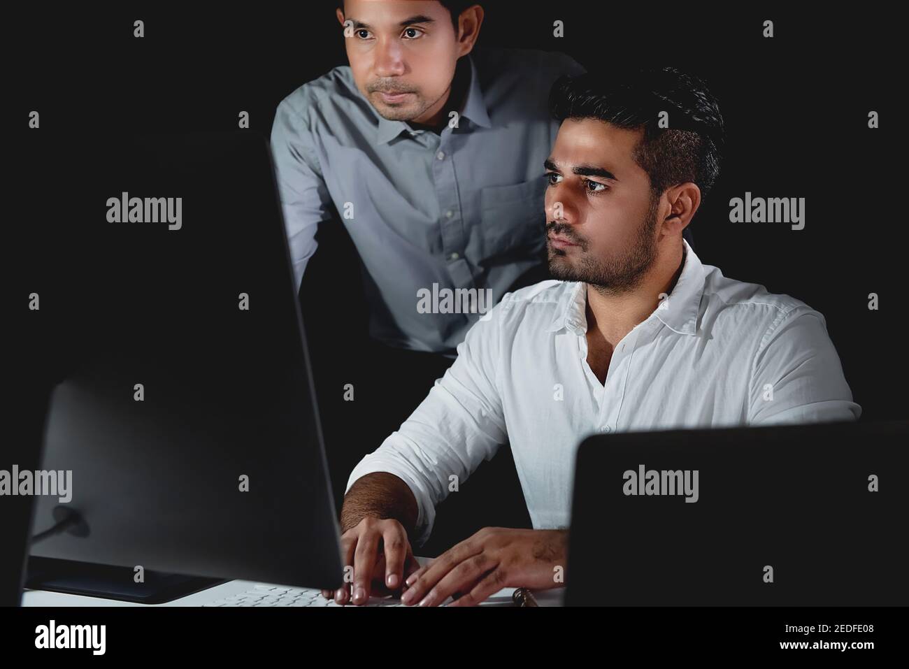 I colleghi asiatici dell'uomo d'affari che lavorano turno di notte in ufficio concentrandosi sullo schermo del computer Foto Stock