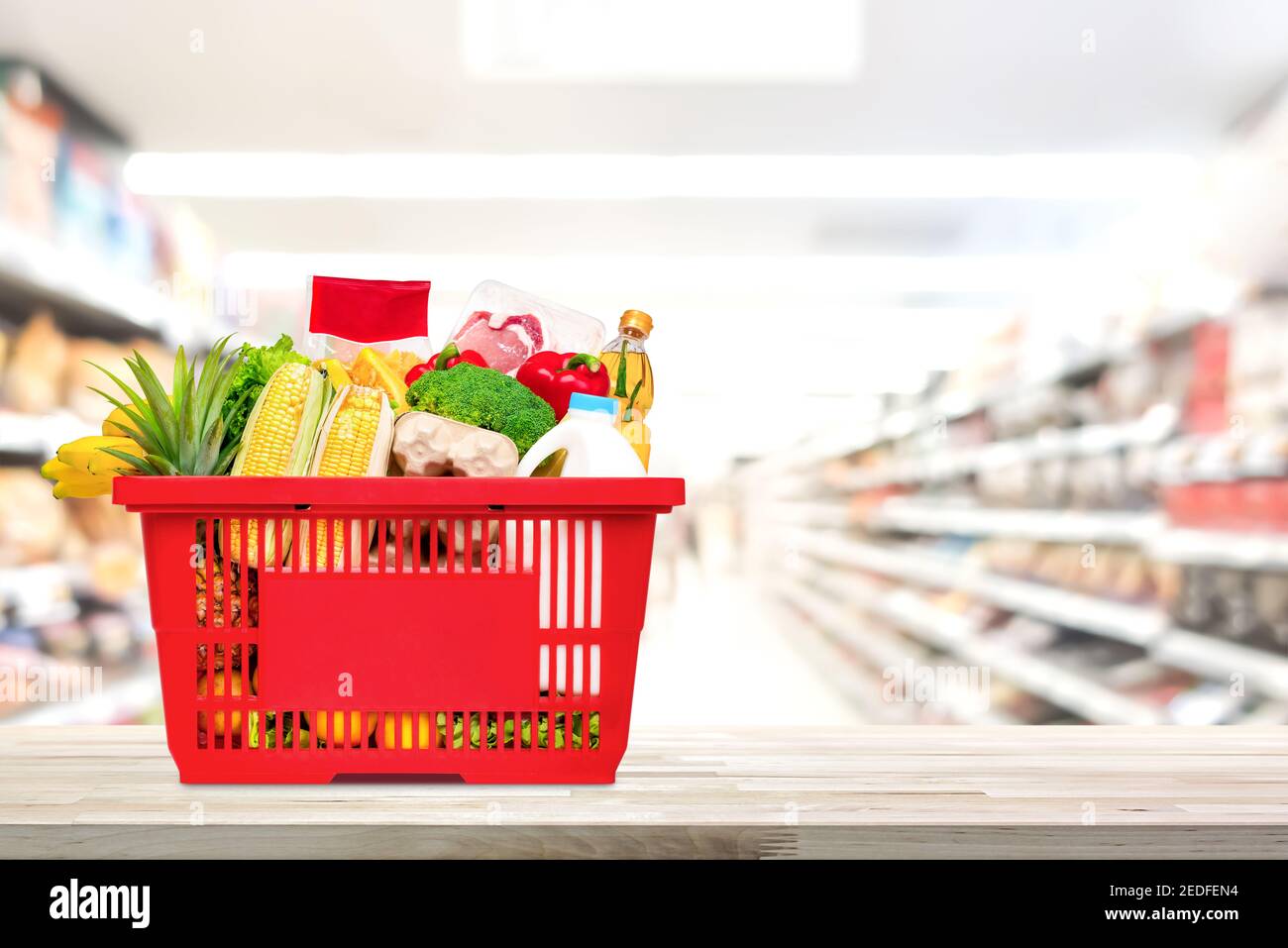 Cibo e generi alimentari in cestino rosso sulla tavola di legno con corridoio del mercato supermarket sfocato in background Foto Stock