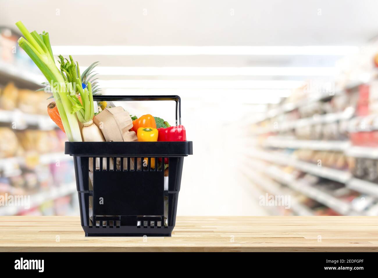 Cibo e generi alimentari in cestino nero su tavola di legno con corridoio del mercato supermarket sfocato in background Foto Stock