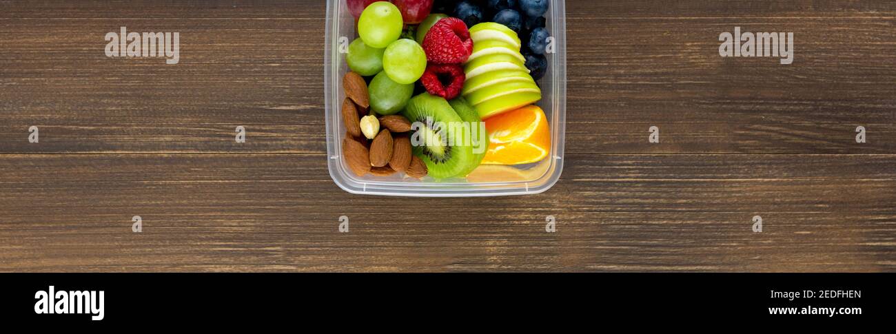 Frutta fresca e sana, colorata e mescolata con mandorle in scatola da asporto banner in legno vista dall'alto Foto Stock