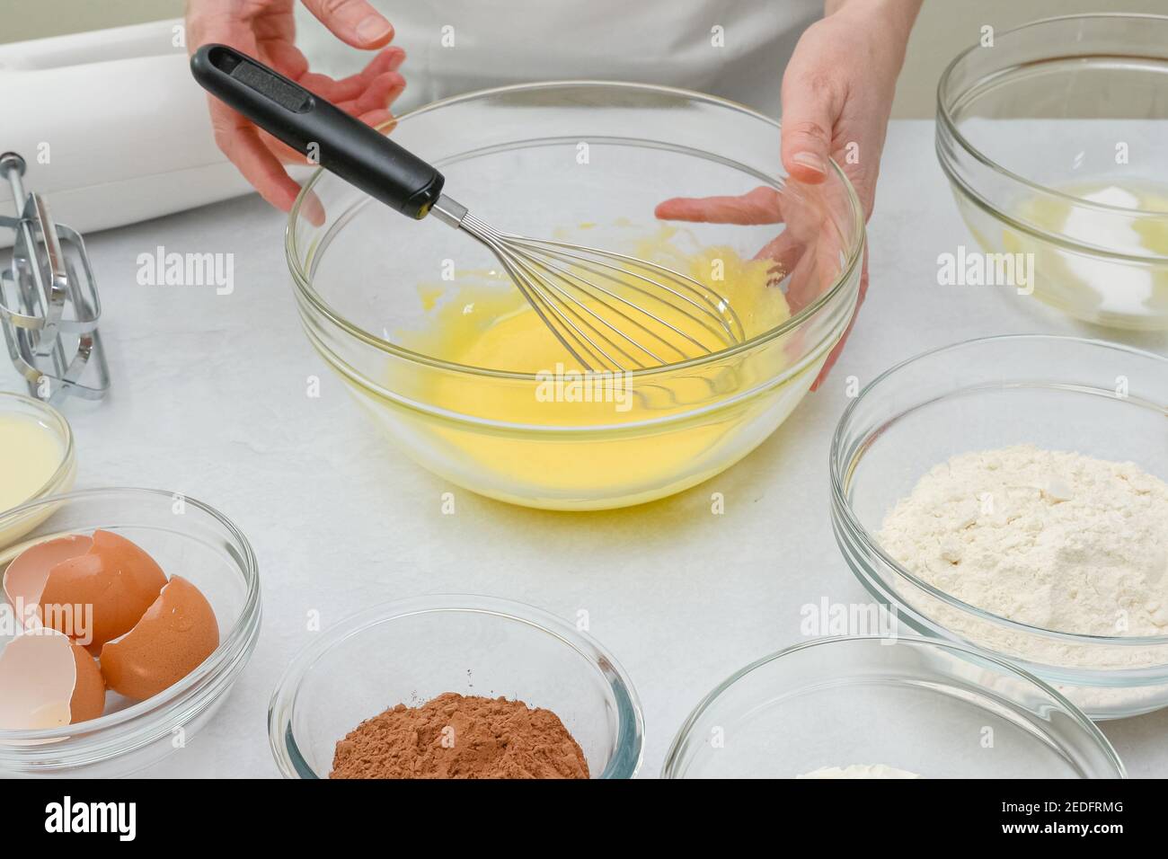 Torta di cioccolato passo dopo passo ricetta. La donna sbatte i tuorli d'uovo con lo zucchero in un recipiente di vetro, primo piano il processo di preparazione Foto Stock