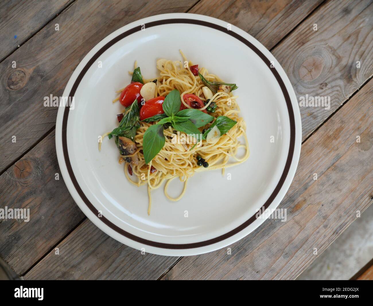 Spaghetti misti con pesce salato con peperoncino al basilico e pomodoro rosso, fusion food italiano in un piatto bianco su tavola di legno marrone Foto Stock