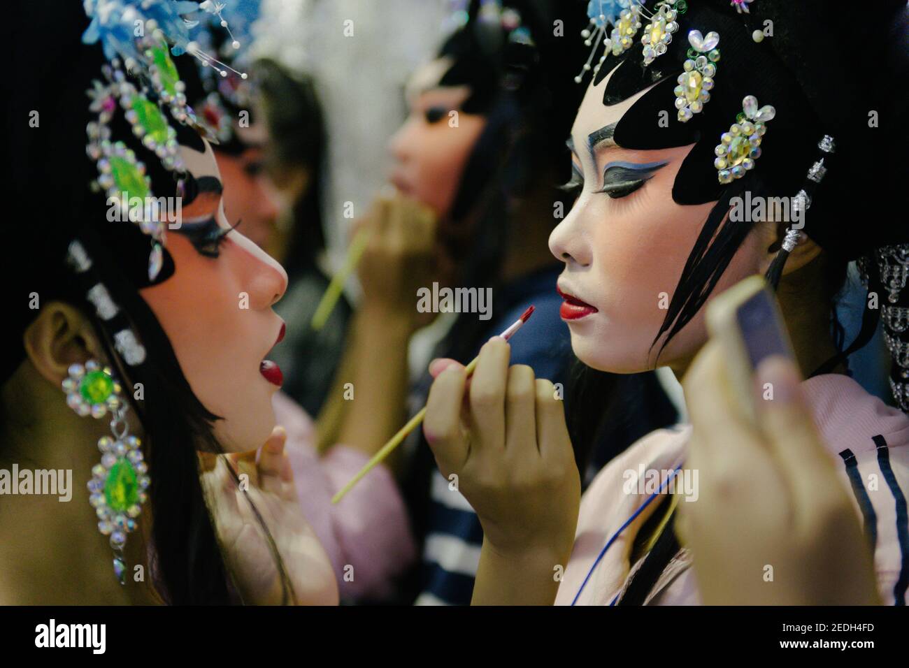 Un profilo closeup di una giovane bella operista cinese in un magnifico costume da fata, mentre la sua amica spazzolando le labbra con un pennello rossetto. Foto Stock