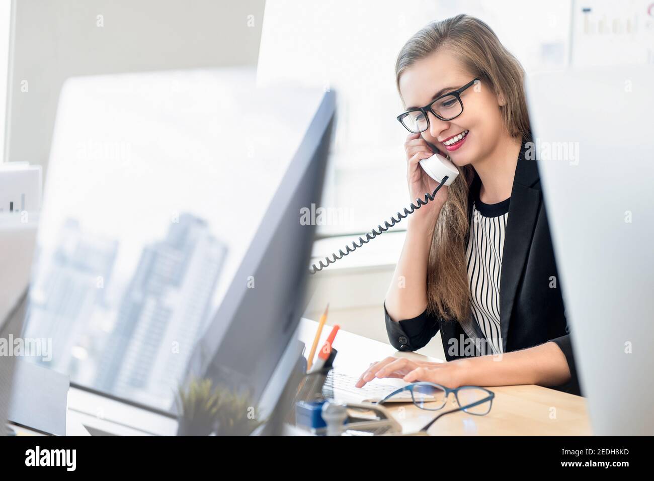 Donna d'affari felice come rappresentante di assistenza clienti che parla su telefono al lavoro con il suo cliente in ufficio Foto Stock