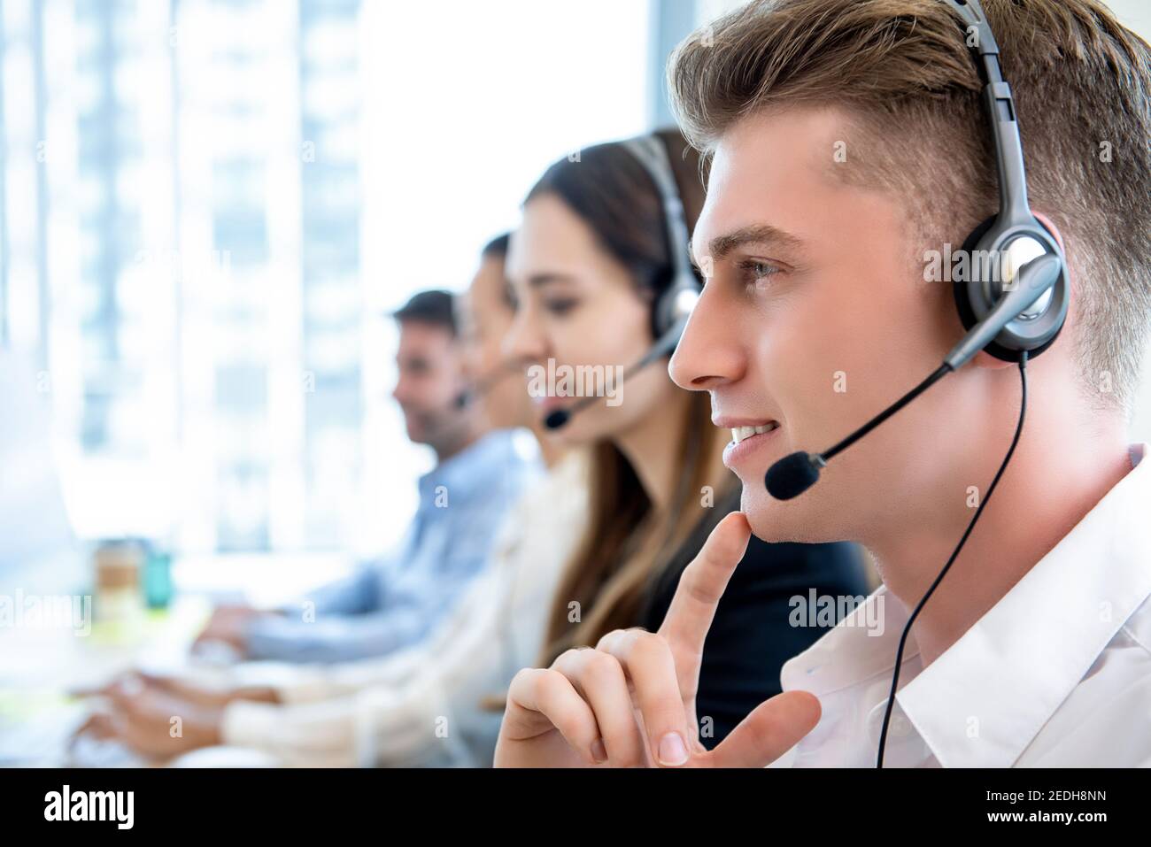 Uomo sorridente e cordiale che lavora in ufficio presso il call center con il team come agente di assistenza clienti per telemarketing Foto Stock