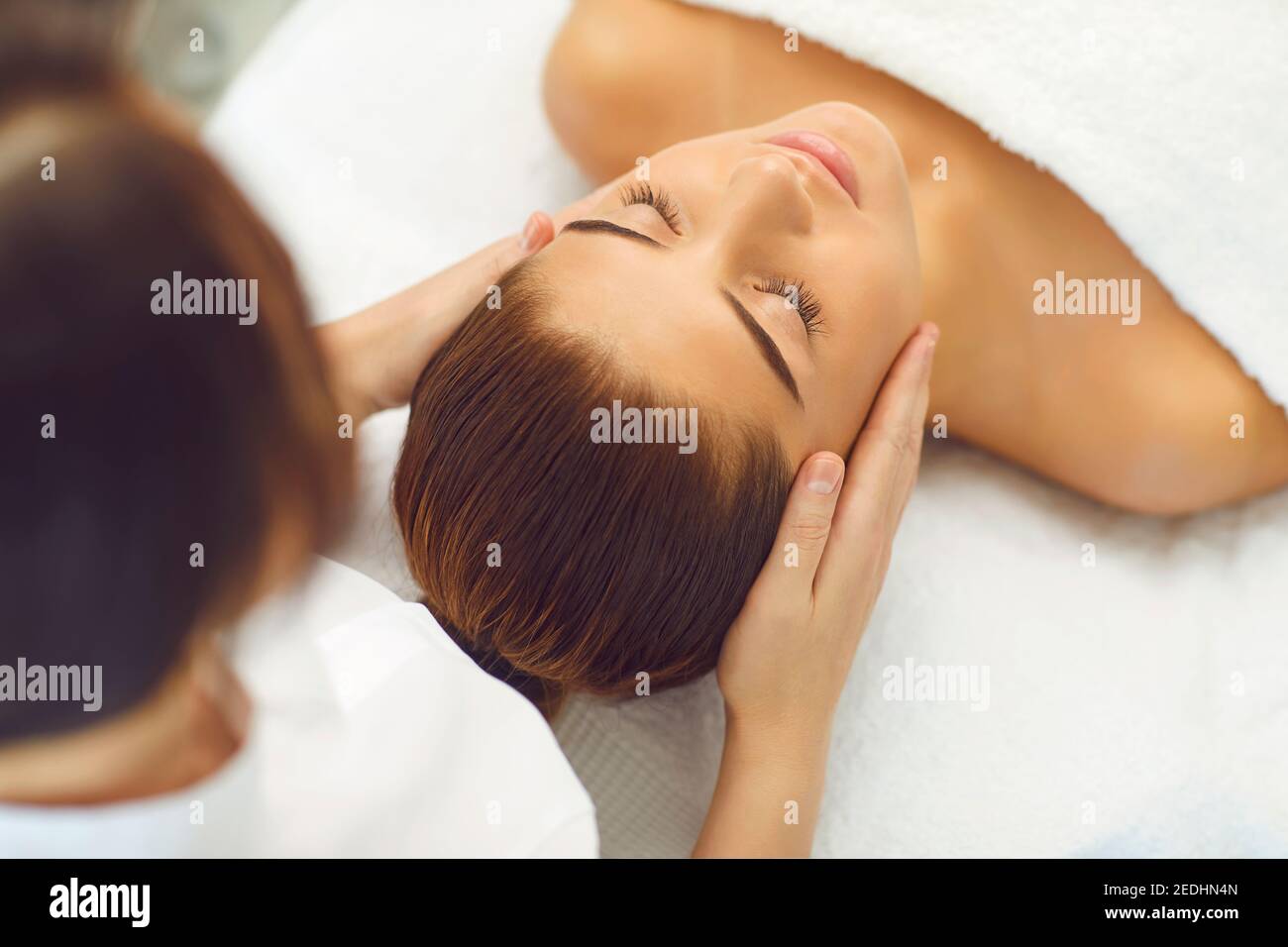 Chiudi le mani di una giovane massaggiatrice che fa il massaggio del viso alla bella donna presso il centro benessere. Foto Stock