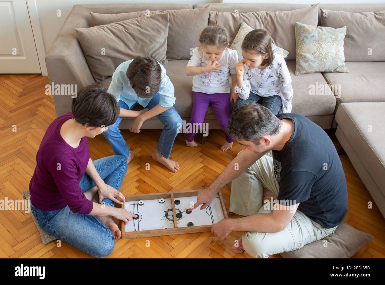 Gioco di gioco di tutta la famiglia. padre e madri corrispondono. Genitori che giocano. Seduto sul pavimento al centro del soggiorno per giocare. Foto Stock