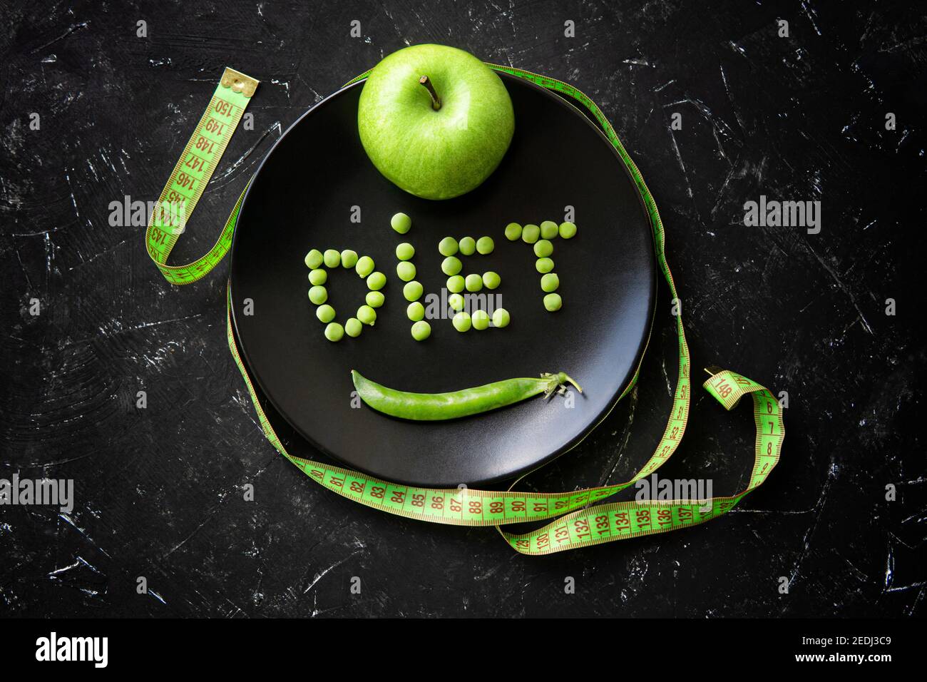 Dieta di parola composta di piselli freschi su un piatto nero, una mela verde intera e una misura di nastro morbido su un tavolo nero testurizzato. Vista dall'alto, spazio di copia. Organi Foto Stock
