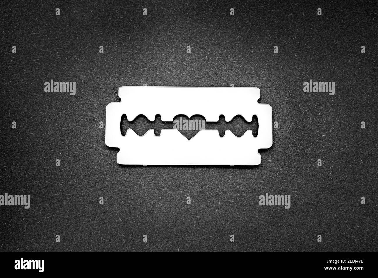 La lama del rasoio a superficie speculare con un'apertura a forma di cuore nella al centro su uno sfondo nero Foto Stock