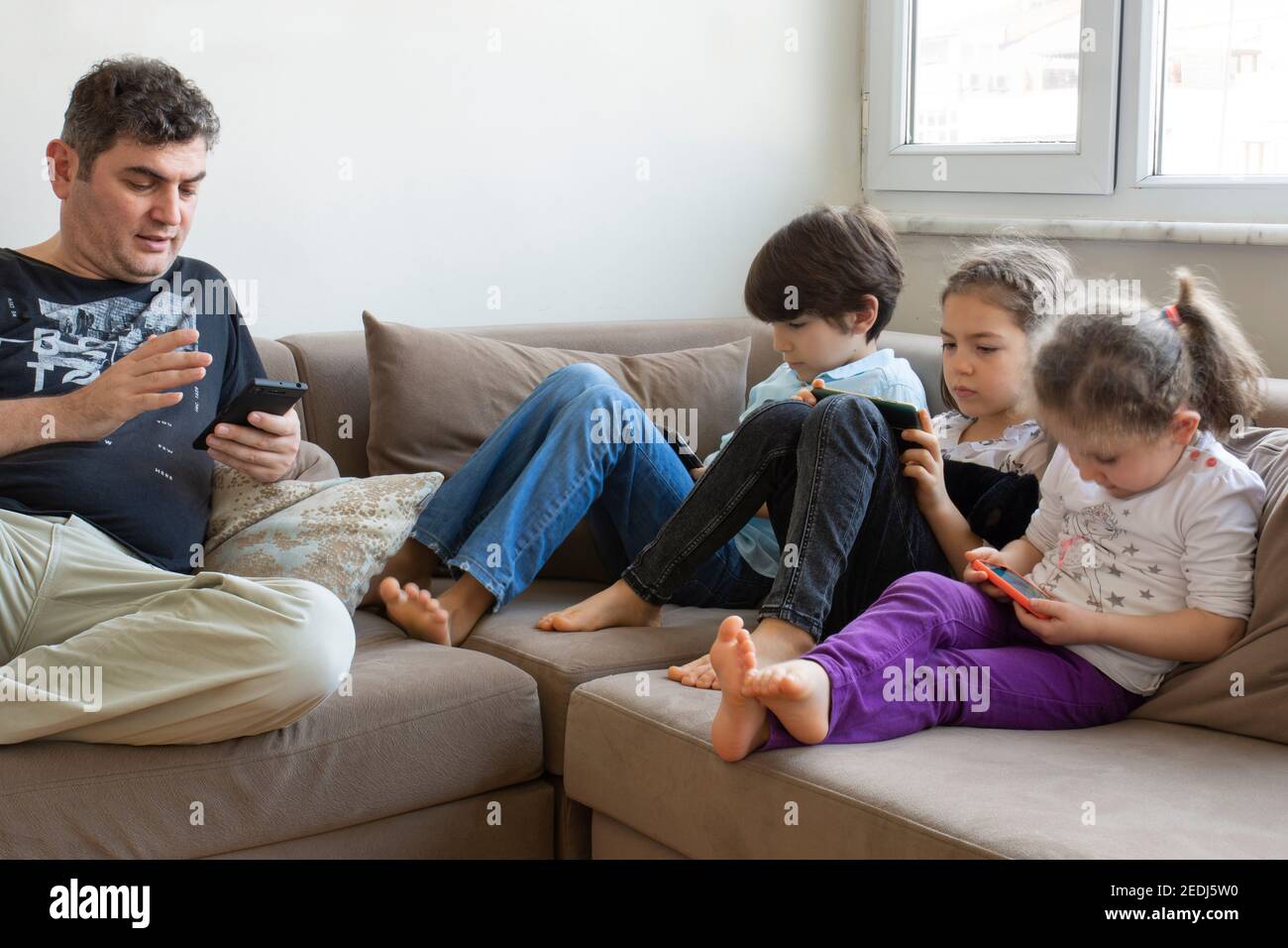 padre e i suoi figli sono seduti sul divano. Giocare a giochi su internet, hanno tutti telefoni cellulari e tablet digitali nelle loro mani Foto Stock