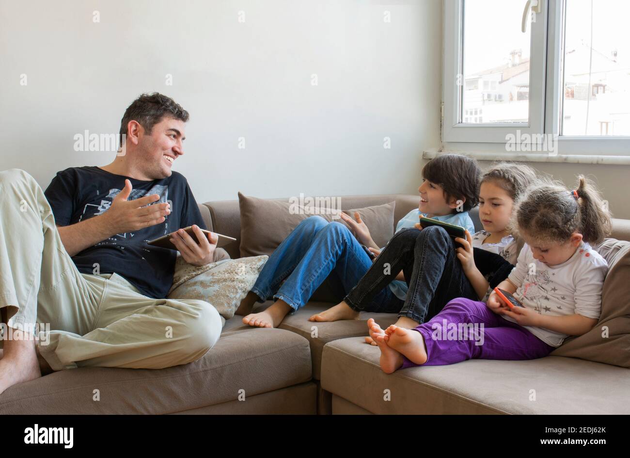 padre e i suoi figli sono seduti sul divano. Giocare a giochi su internet, hanno tutti telefoni cellulari e tablet digitali nelle loro mani Foto Stock