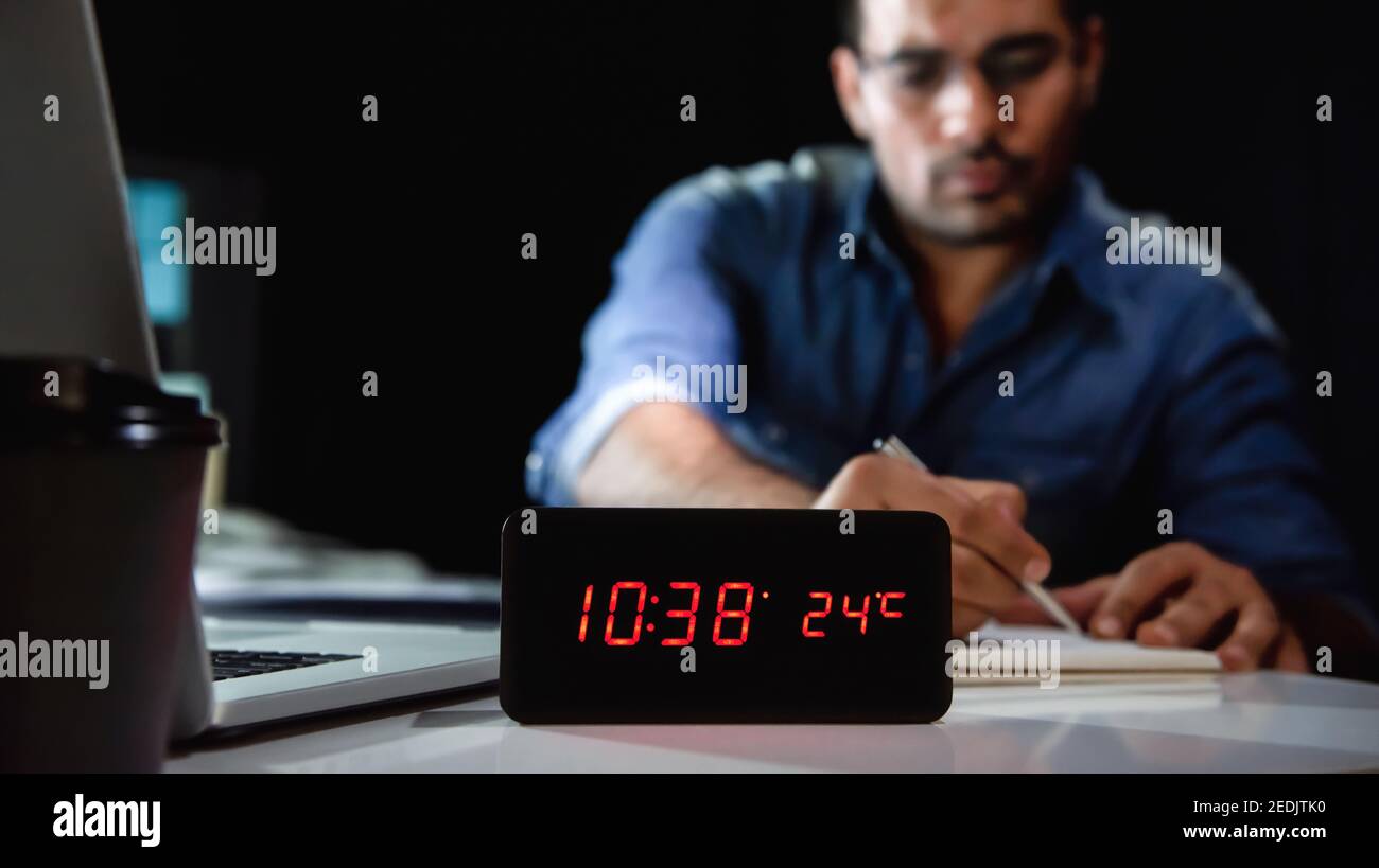 Uomo lavorante che rimane in orario straordinario a tarda notte in ufficio lavorare alla sua scrivania Foto Stock