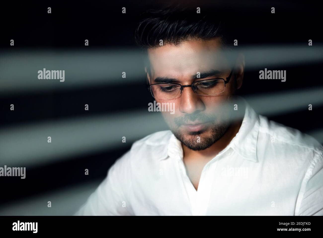 Uomo d'affari asiatico informale che rimane fuori orario fino a tarda notte lavorando dentro l'ufficio dietro il divisorio di vetro Foto Stock