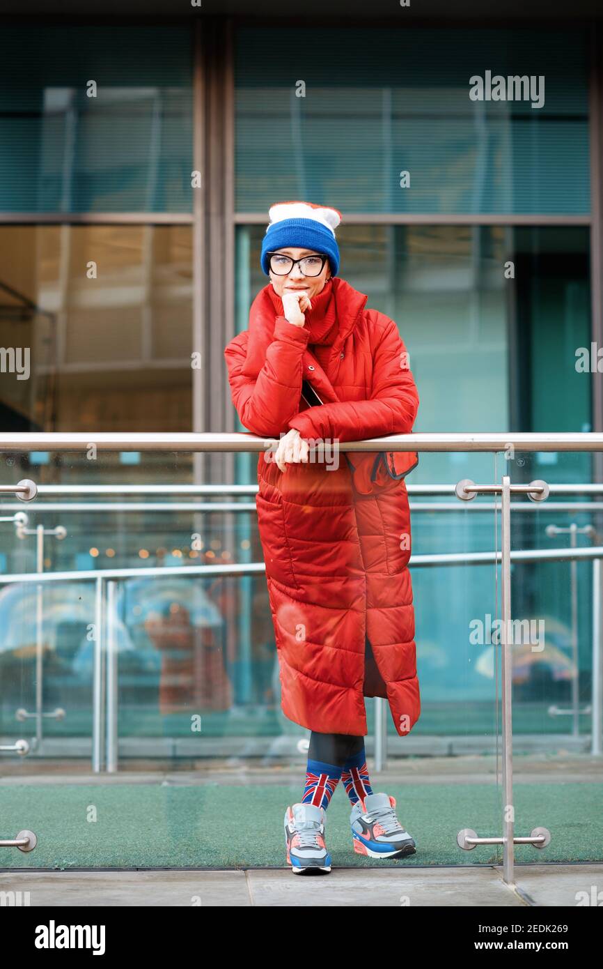 donna felice in cappotto rosso, cappello che cammina per la città in tempo freddo Foto Stock