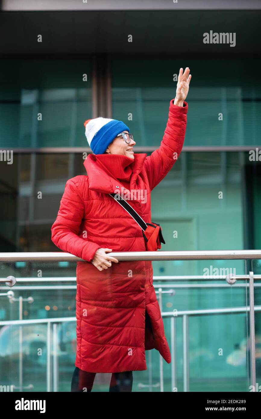 donna felice in cappotto rosso, cappello che cammina per la città in tempo freddo Foto Stock