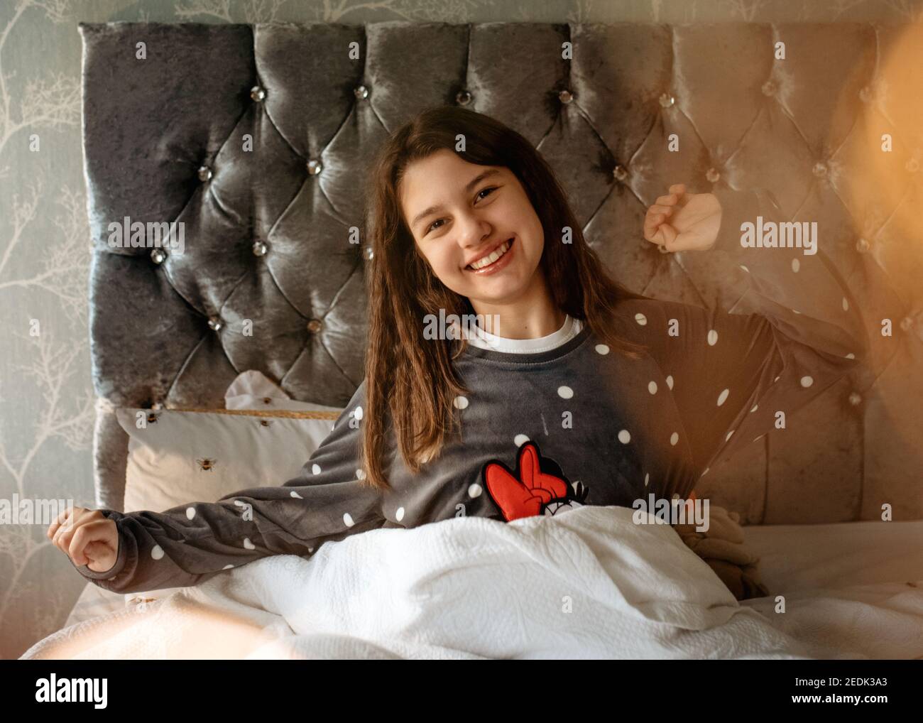 Sorridenti ragazze in pigiami grigi che giacciono e scivolano sul letto e abbracciare un gatto al mattino Foto Stock