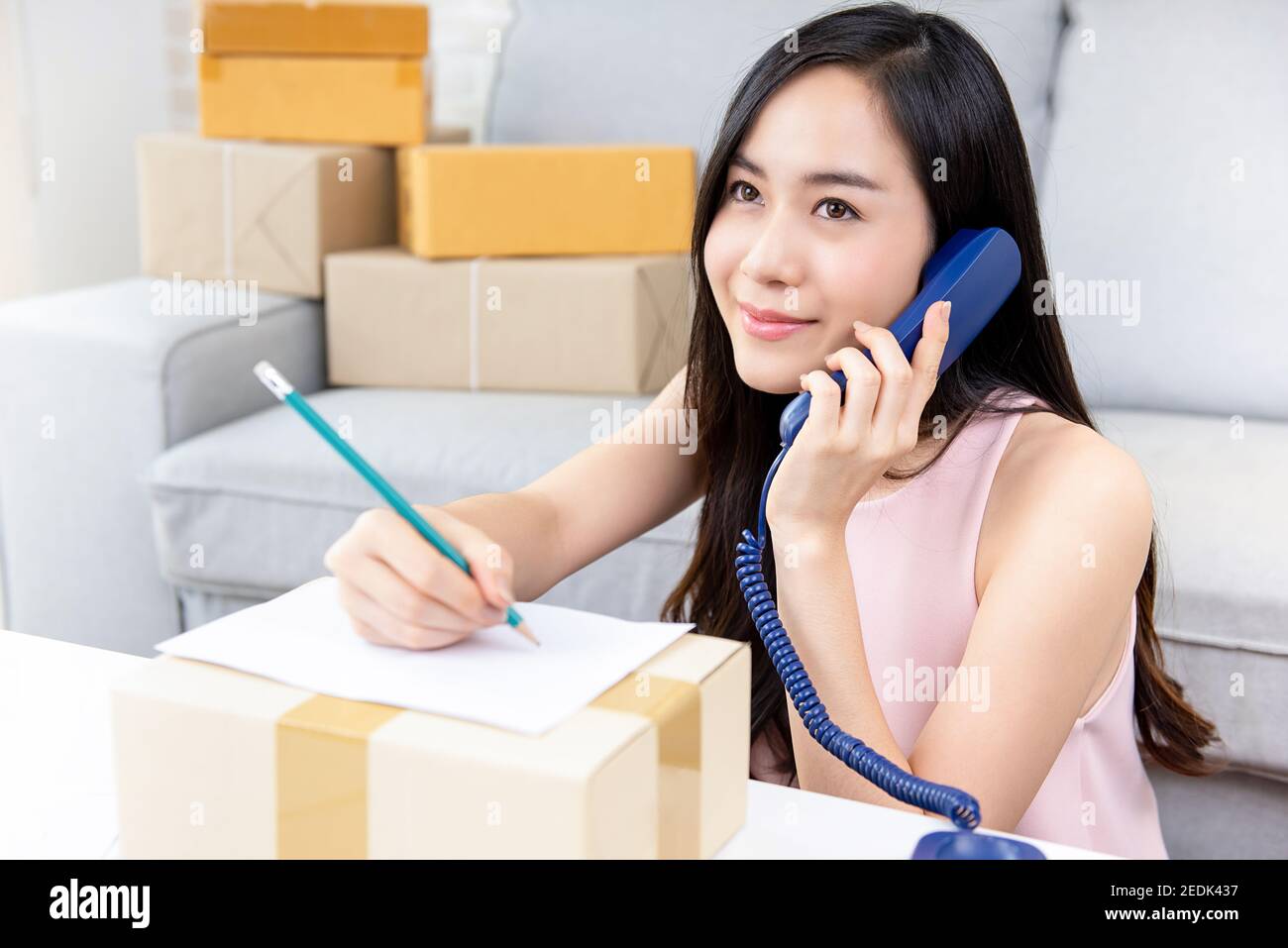 Giovane imprenditore asiatico di donna o venditore online freelance che lavora a. chiamata a casa del cliente al telefono per confermare gli ordini prima consegna Foto Stock