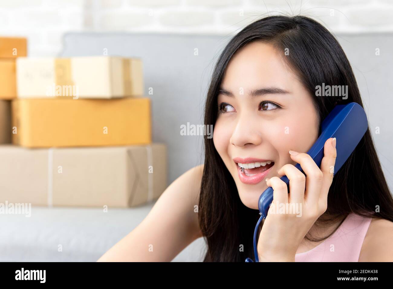 Giovane imprenditore asiatico di donna o venditore online freelance che lavora a. chiamata a casa del cliente al telefono per confermare gli ordini prima consegna Foto Stock