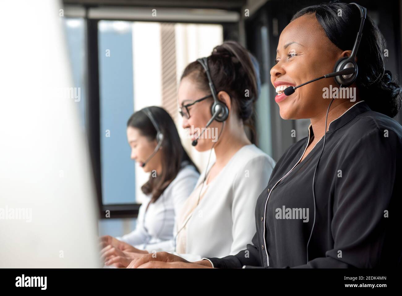 Donna nera accogliente che indossa cuffie con microfono che lavorano nel call center con team internazionale come agenti di telemarketing per il servizio clienti Foto Stock