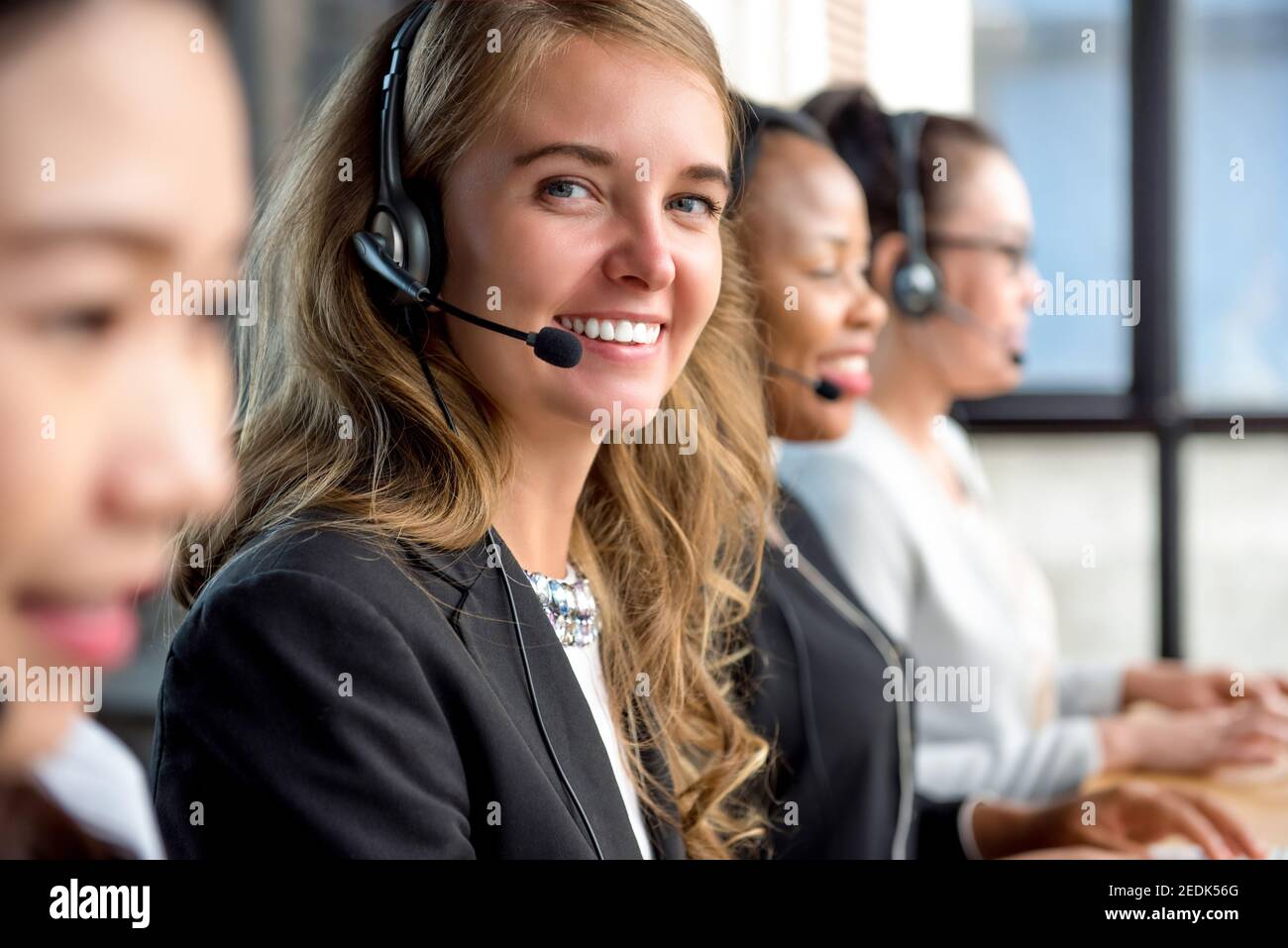 Gentile bella donna caucasica telemarketing agente di servizio di cliente che lavora dentro call center con il suo team multietnico Foto Stock