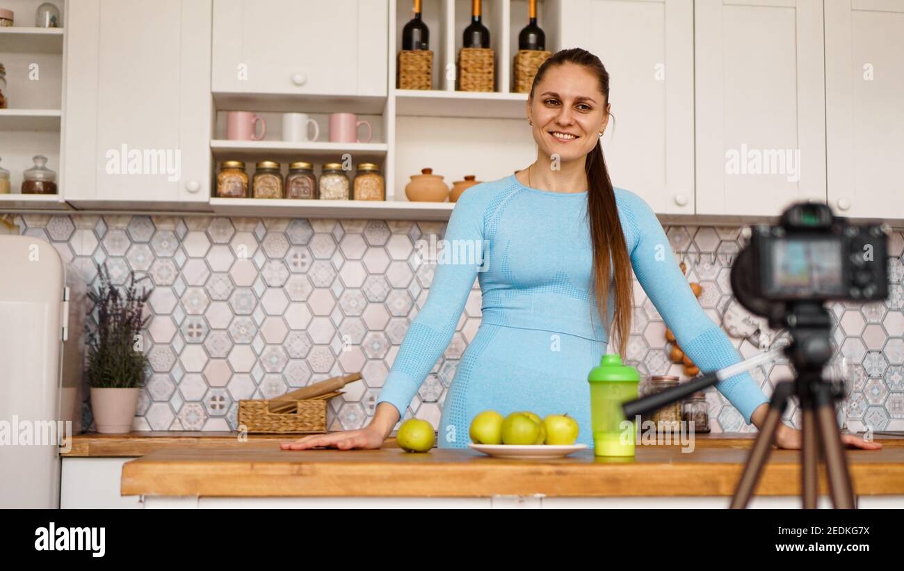 Soddisfatta giovane ragazza sana che registra il suo video blog episodio su cibo sano mentre si trova in cucina a casa. Donna è amichevole e sorridente Foto Stock