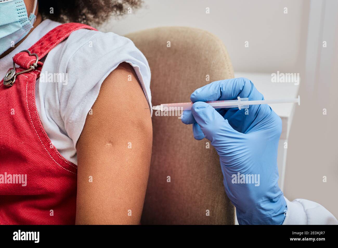 Corto di spalla della bambina durante l'iniezione del vaccino in una clinica medica. Pandemia globale Foto Stock