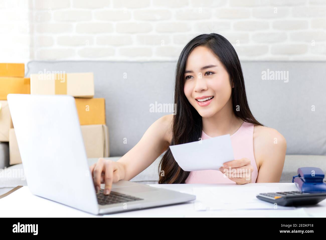 Giovane donna asiatica imprenditore o freelance venditore online che lavora su computer portatile verifica ordine su internet a casa preparazione per consegna Foto Stock