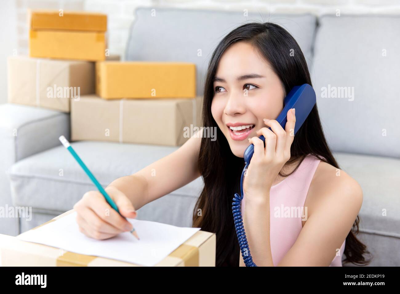 Giovane imprenditore asiatico di donna o venditore online freelance che lavora a. home conferma ordini da parte del cliente al telefono per la preparazione consegna Foto Stock