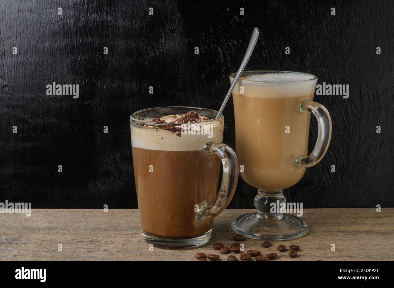 Due tazze in vetro con cappuccino e cioccolato ghiacciato su un tavolo di legno con fondo a trama nera. Messa a fuoco selettiva. Foto Stock
