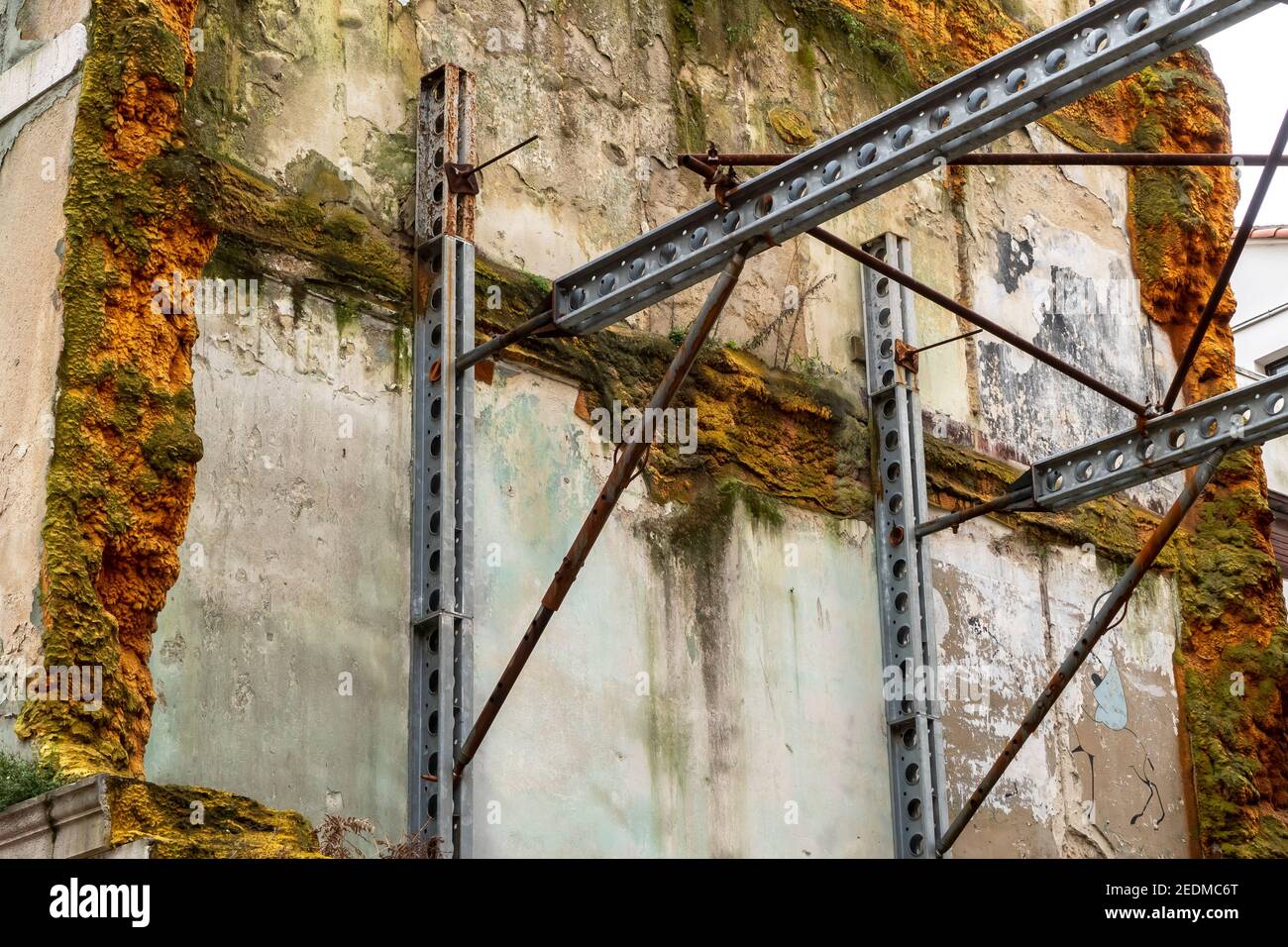 Vecchia parete mussosa danneggiata di un edificio distrutto sigillato con schiuma, sostenuta da travi di montaggio in acciaio Foto Stock