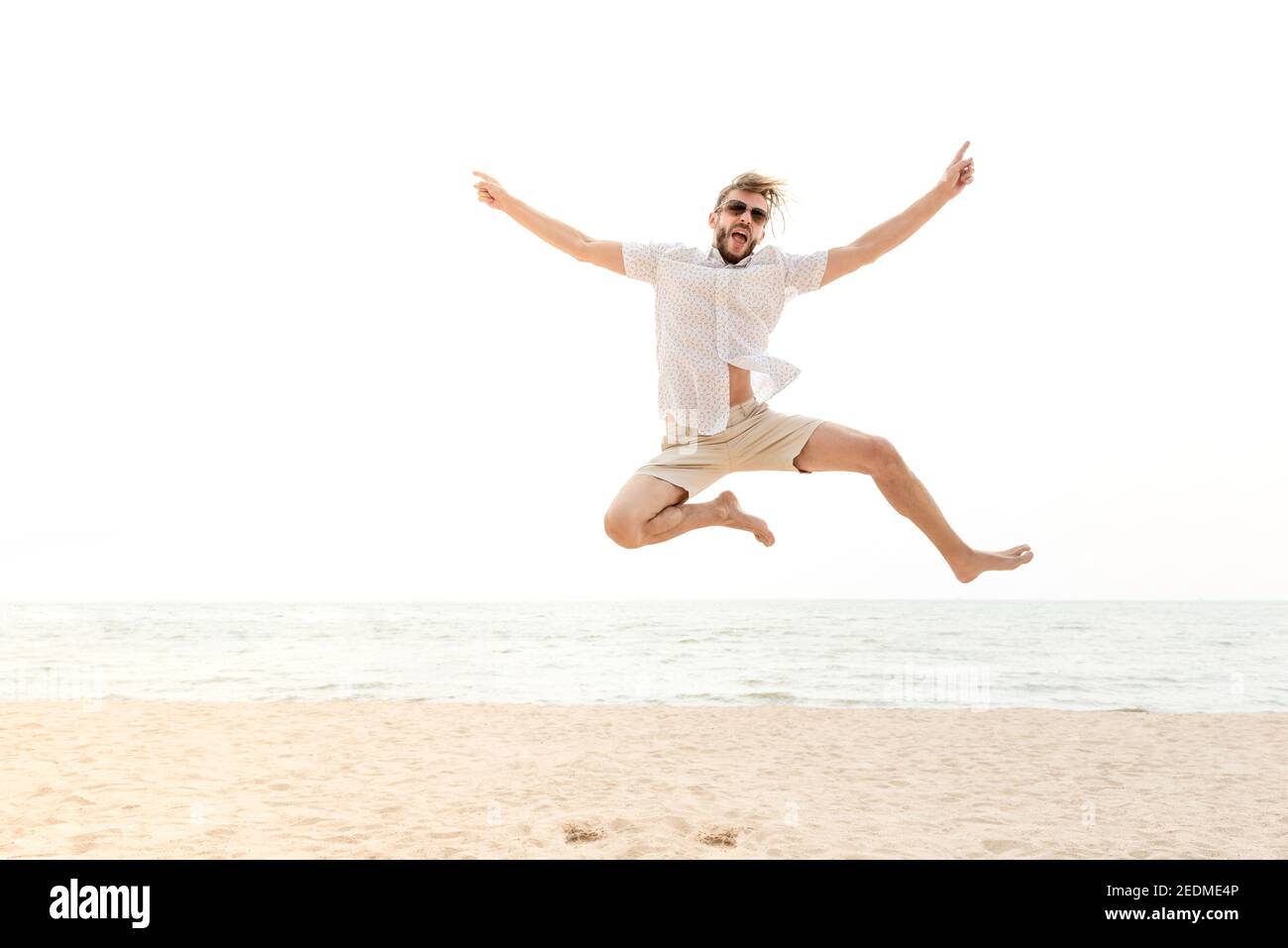 Giovane energico felice uomo turistico che salta in spiaggia per le vacanze estive, divertimento e concetti di libertà Foto Stock