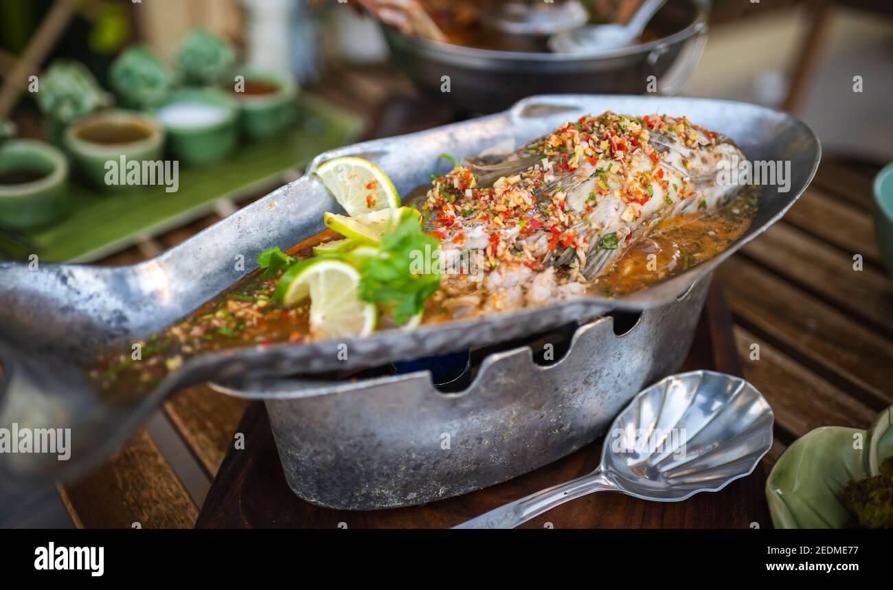 Pesce amour al vapore con pepe di lime e vari ingredienti alimentari Su un tavolo con piatti thailandesi Foto Stock